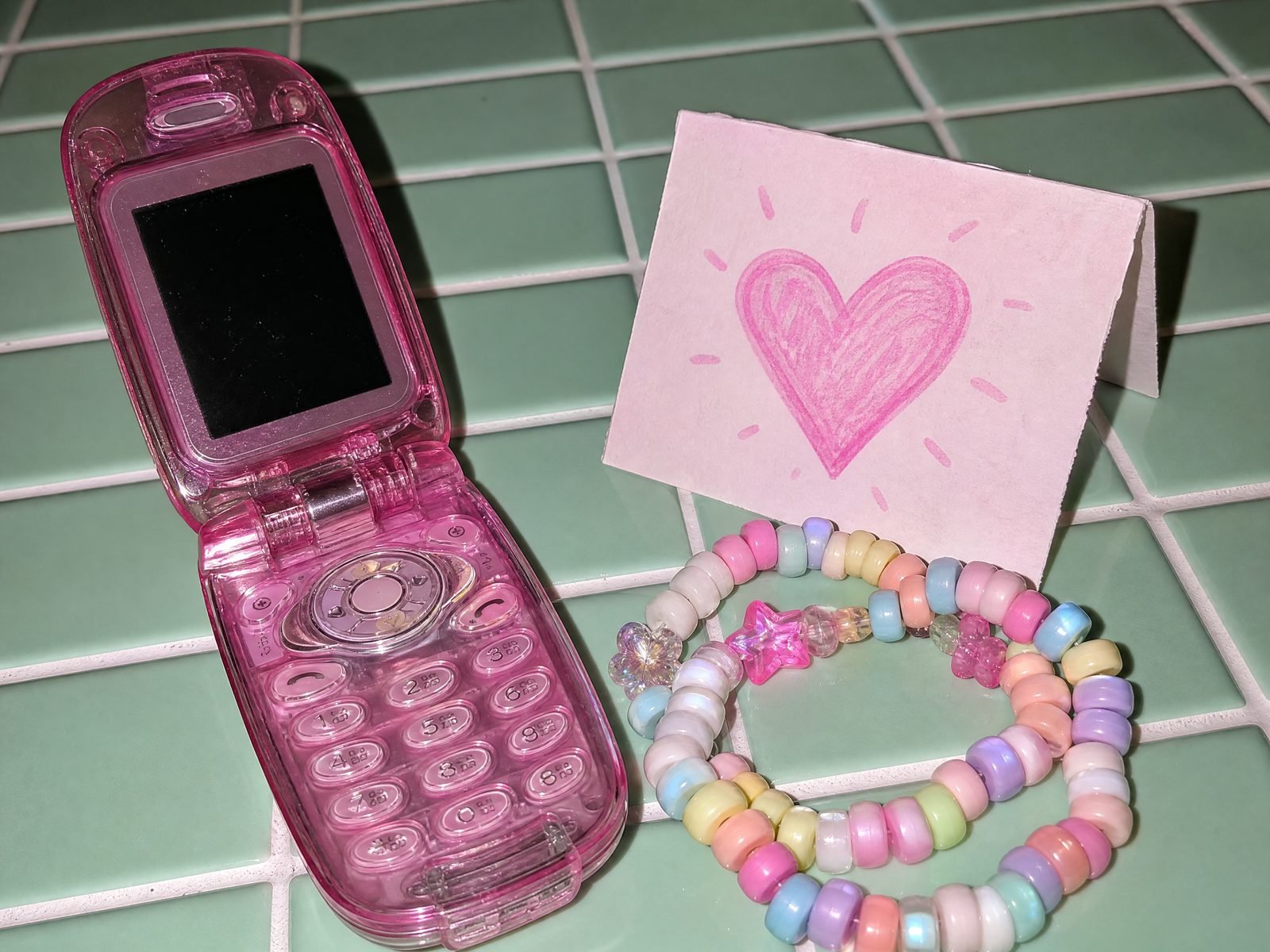 Pink flip phone and bead bracelets on mint tiles